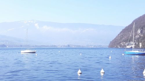 Sailboats moored in sea by mountain against sky