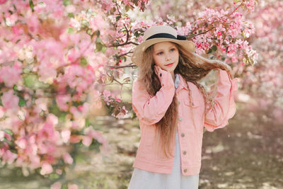 Portrait of beautiful young woman standing by pink flower tree