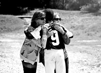 Rear view of teenage boy embracing mother and grandmother on field