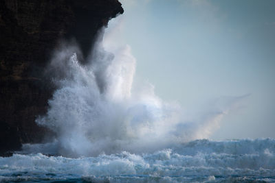 Sea waves splashing on rocks against sky