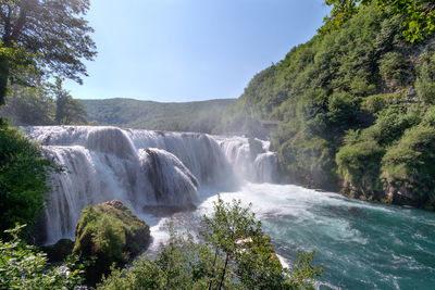 Scenic view of waterfall in forest against clear sky