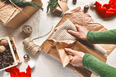 Woman's hands wrapping woolen sweater in craft recycled paper on the table with christmas decoration