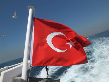 Red flag on sea against blue sky