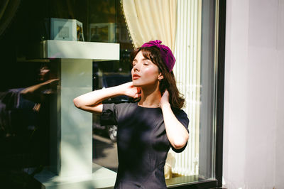 Beautiful young woman in black dress standing by building