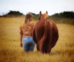 Rear view of woman standing by horse on field