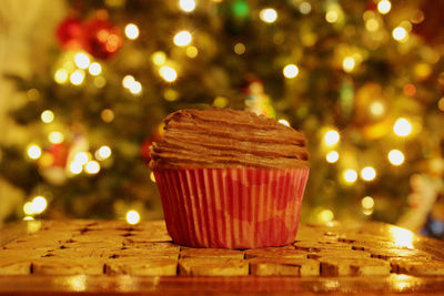 Close-up of cupcake on table against illuminated christmas tree