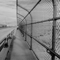Rear view of man walking in bridge by chainlink fence