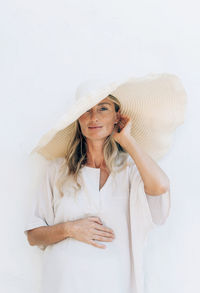 Portrait of a beautiful pregnant woman in white clothes and a large tropical hat.