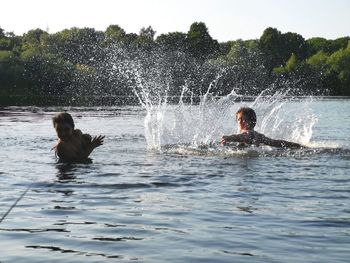 Men in water splashing against sky