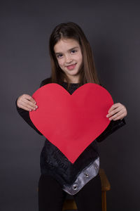 Portrait of woman holding heart shape over black background