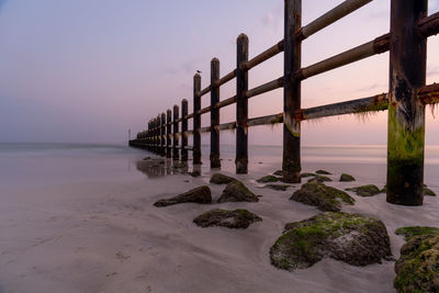 Pier on beach against sky during sunset