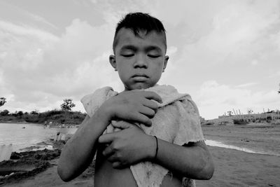 Close-up of boy standing at beach against cloudy sky