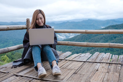 Full length of woman using laptop at observation point against sky