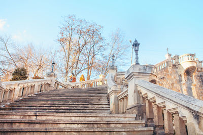 Elegant stone staircase with ornate balustrades and vintage lampposts, leading upward 