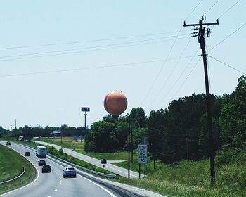 Road by electricity pylon against sky