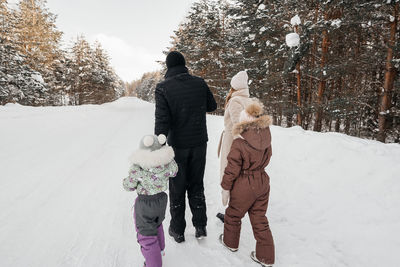 Dad and mom and two daughters walk through the snowy forest