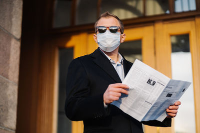 Businessman wearing mask while standing with newspaper in city