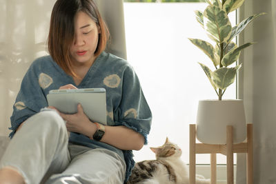 Asian woman play with her cat and use tablet meeting and working from home