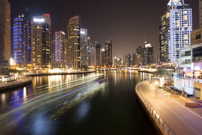 Illuminated buildings by river against sky at night