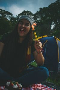 Smiling woman holding lit sparkler against trees