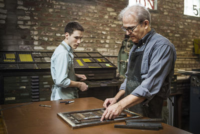Worker arranging letterpress equipment on workbench in workshop