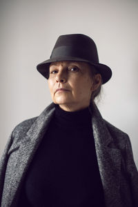 Fashionable older woman in black clothes and a hat stands against a white wall in the office