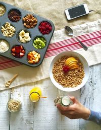 Directly above shot of hand holding milk by breakfast cereals on table