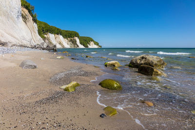 Scenic view of beach amidst mountain against clear blue sky during sunny day