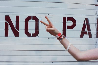 Cropped hand of woman gesturing peace sign against shutter