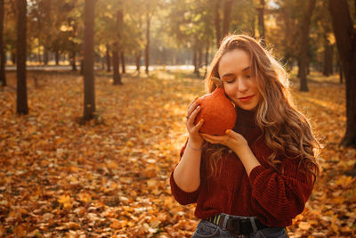 Young beautiful smiling woman with long curly hair holding orange halloween pumpkin on autumn park 