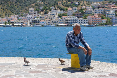 Full length of man sitting on sea by city