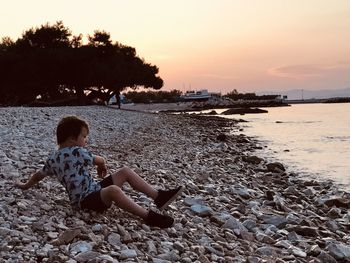 Boy sitting on the beach throwing rocks in the sea during sunset