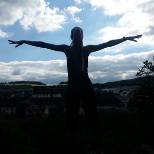 Woman with arms outstretched standing against sky