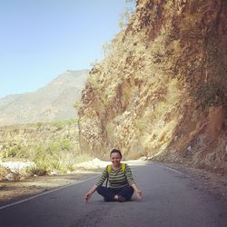 Portrait of smiling woman doing yoga on road against mountains