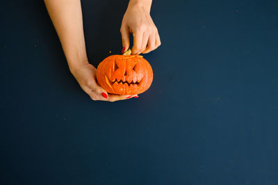 Low angle view of hand holding pumpkin against blue background