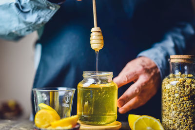 Midsection of woman holding wooden honey stick and jar with organic honey