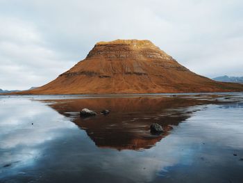 Scenic view of kirkjufell reflection in water against cloudy sky