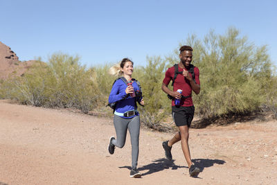 Hikers running on field against clear sky during sunny day