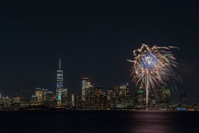 Firework display over illuminated buildings against sky at night