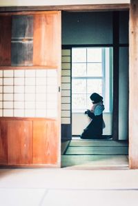 Side view of woman standing against window