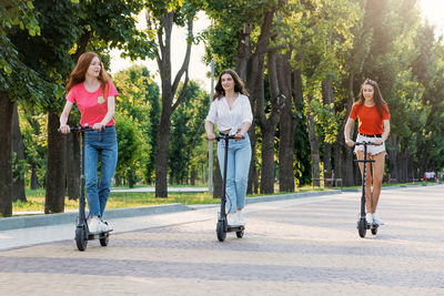 Three young girl friends on the electro scooters having fun in city street at summer sunny day. 