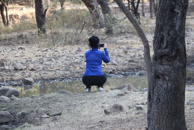 Rear view of man photographing on tree trunk