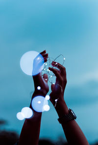 Cropped hands holding illuminated lights against sky