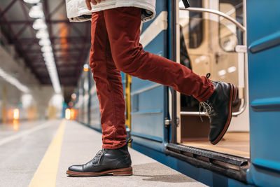 Attractive man in black shoes, burgundy pants and white jacket gets out of subway wagon. 