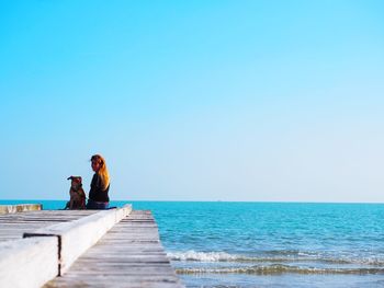 People sitting on beach against clear blue sky