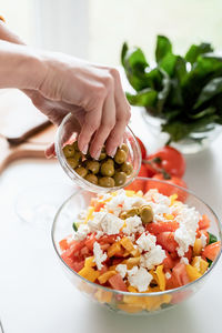 Healthy eating. female hands making greek salad adding olives to the bowl