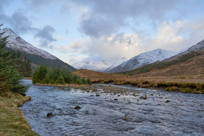 Scenic view of stream by mountains against sky