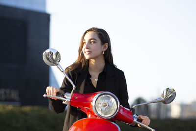 Businesswoman looking away while sitting on motor scooter during sunset