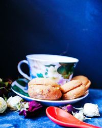 Close-up of cookies in saucer with flowers on table against blue background