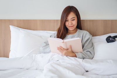 Portrait of young woman using mobile phone while lying on bed at home